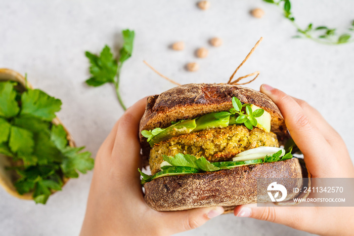 Vegan sandwich with chickpea patty, avocado, cucumber and greens in rye bread in children’s hands.