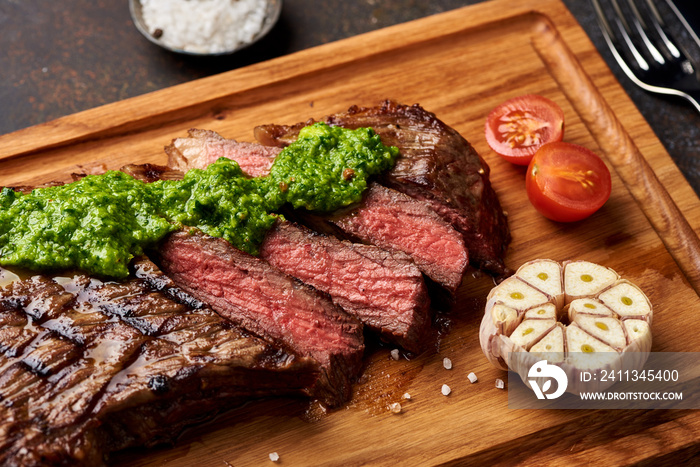 Grilled Black Angus Steak with tomatoes, garlic with chimichurri sauce on meat cutting board.