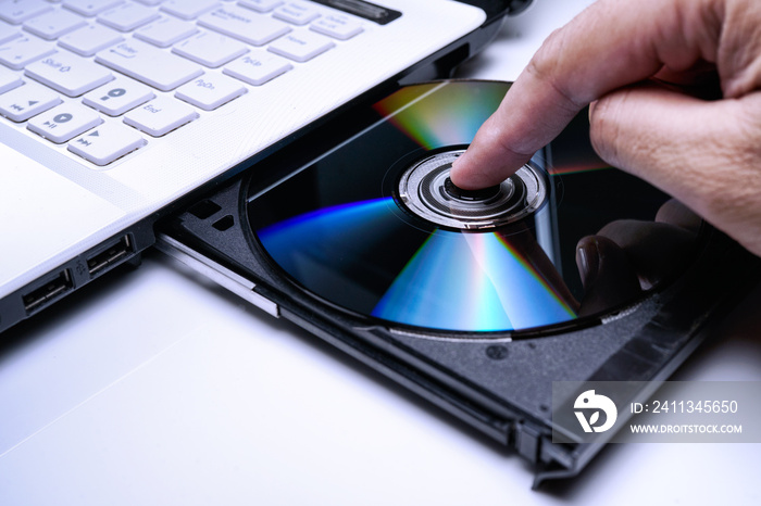 DVD Disk on the white Laptop DVD ROM Tray with a Man Hand. A Piracy conceptual image of burning data into DVD Disk