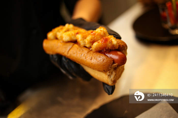 cook in black gloves holds hot dog. The cook prepares a hot dog, adding the sauce to the sausage. hamburgers, hot dog. concept of fast food. cook hot-dog