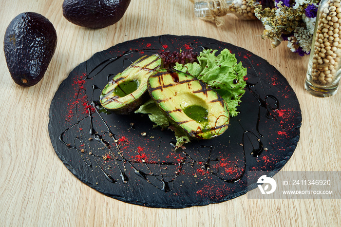 Sliced Grilled avocado on black slate board with spices and black sauce. Close up view. Healthy food for lunch