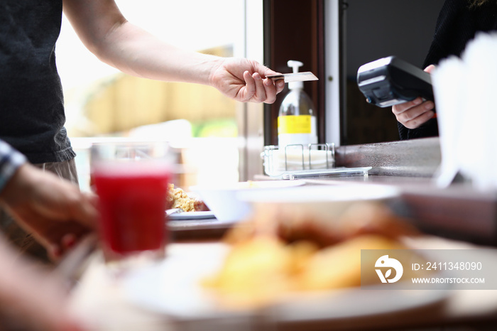 Man’s hand holds out contactless bank card to cashier to pay for lunch. Payments by term in public places