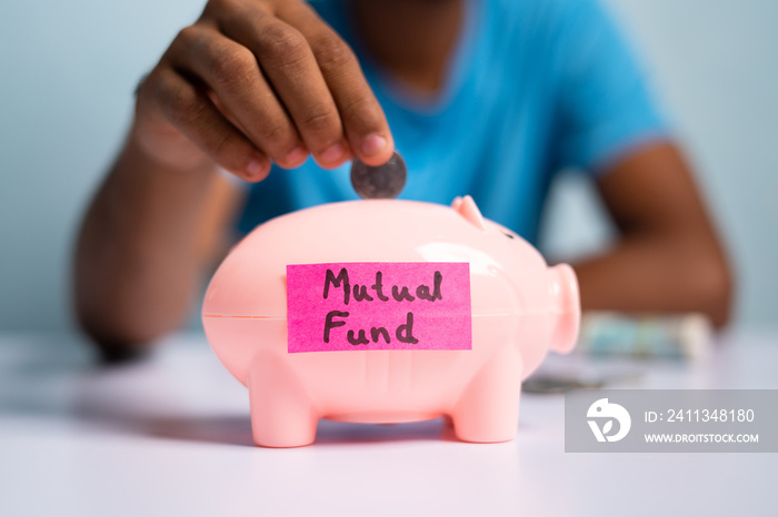 Concept of mutual fund investment, showing with hands placing coins inside the piggy bank with mutual fund sticker