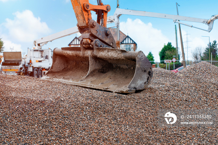 Excavator bucket on top of gravel with concrete pump in background awaiting concrete delivery