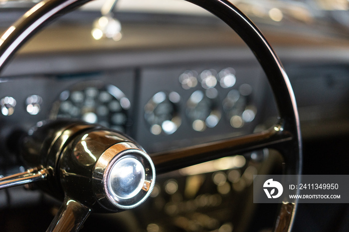 Cockpit eines Oldtimers mit schwarzem großen Lenkrad und bokeh im Hintergrund