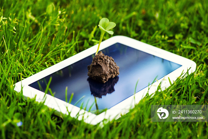 a touch screen of smartphone,tablet,cell phone with seedling growing up on screen over green grass. abstract background to green communication technology concept.