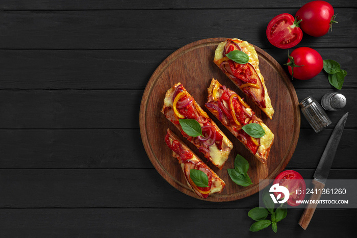 Gluten-Free Pizza Flatbread. Pizza on a flatbread with vegetables on a black wooden background. The pizza cut into slices lies on a wooden stand.