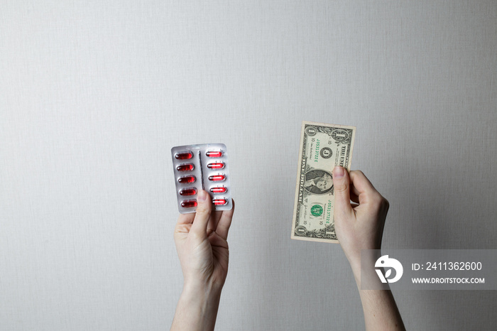 the girl holds medicines in one hand and one dollar in the second.