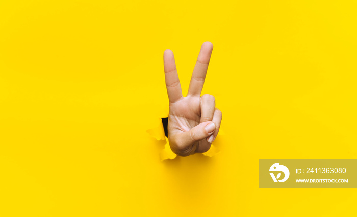 Victory sign two-finger hand gesture on yellow background with torn paper hole and copy space. It is ok concept.