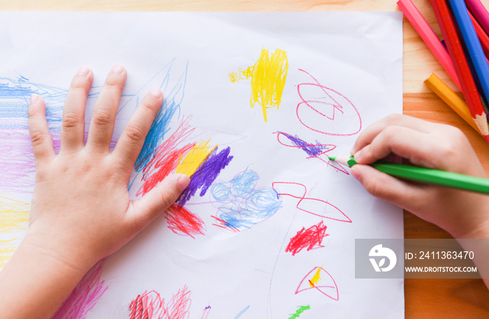 Girl painting on paper sheet with colour pencils on the wooden table at home - child kid doing drawing picture and colorful crayon