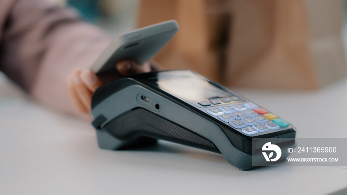 Woman at check-in desk at counter pays with smartphone through NFC contactless payment from mobile phone in bar cafe purchase of food products pay by card from telephone close-up focus on terminal