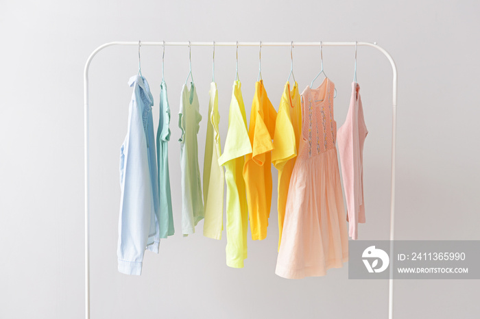 Stylish kid clothes hanging on rack against light background