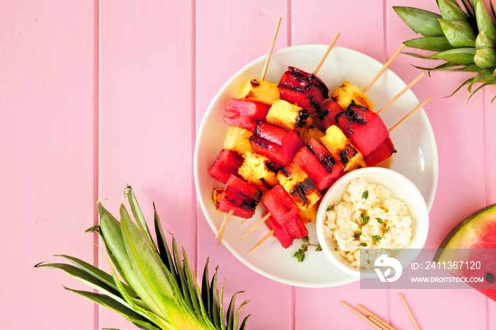 Grilled watermelon and pineapple fruit skewers with feta. Top view on a pink wood background. Summer food concept.