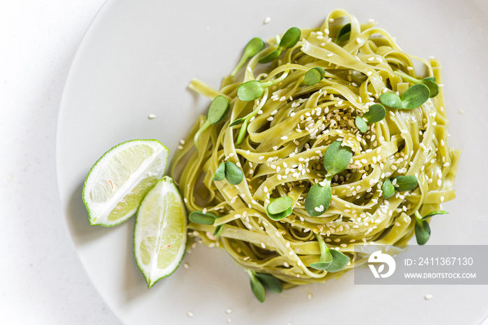 Green vegan spinach pasta with sunflower seeds microgreens, sesame seeds and lime