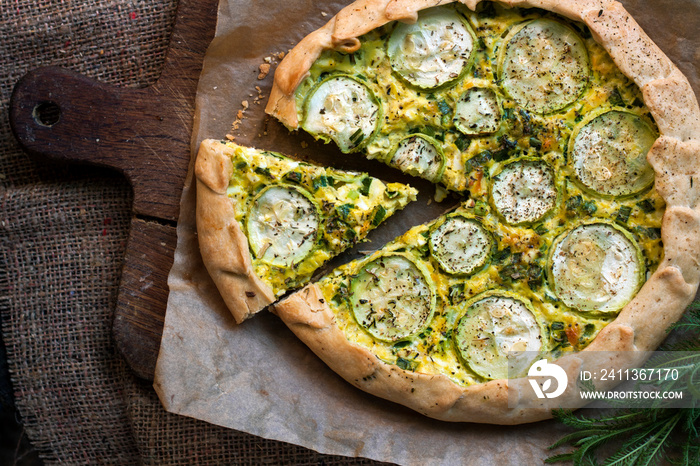 Homemade courgette and goat cheese pie on a dark rustic wooden board background