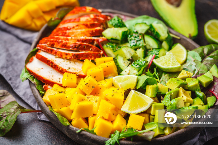 Grilled chicken, mango and avocado salad in dark dish on dark background.