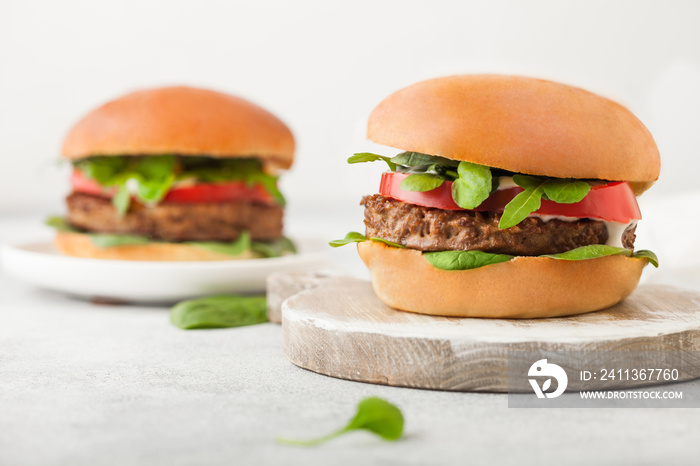 Healthy vegetarian meat free burgers on round chopping board with vegetables and spinach on light table background.