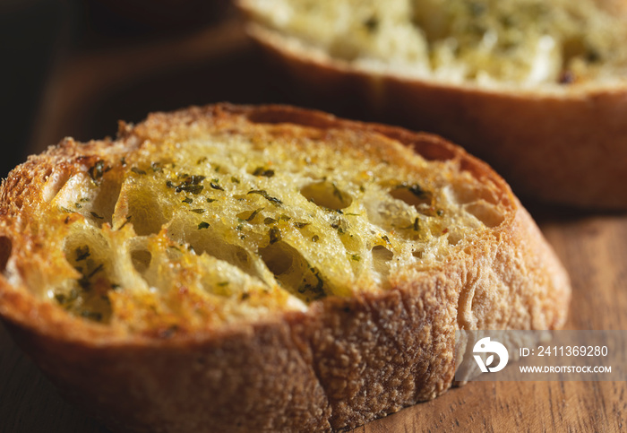 Sliced baked bread with garlic and herbs on a wooden cutting board on the table.