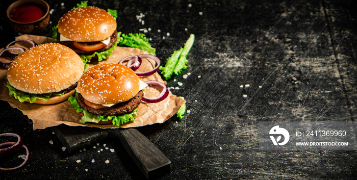 Burger on a cutting board with onion rings, tomato sauce and lettuce.