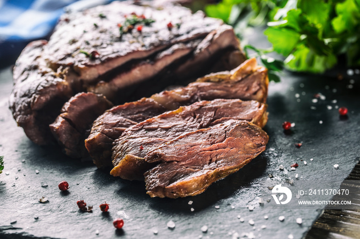 Freshly grilled beef steak on slate plate with salt pepper rosemary and parsley herbs. Sliced pieces of juicy beef steak