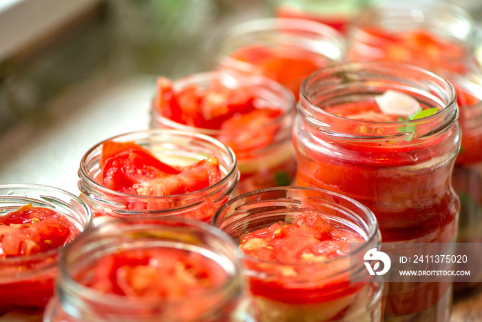 Canning fresh tomatoes with onions for winter in jelly marinade. Macro shot of basil leaves on top of a red ripe tomato slice being put in jar.