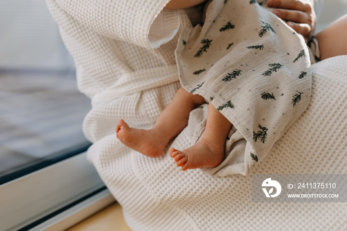 Closeup of barefoot newborn baby feet. Mother holding little child in arms.