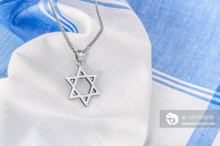 Star of David ( Magen David ) with chain on white-blue fabric.