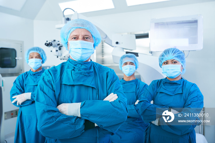 Confident team of surgeons in scrubs, caps and face masks standing with their arms folded and looking at camera