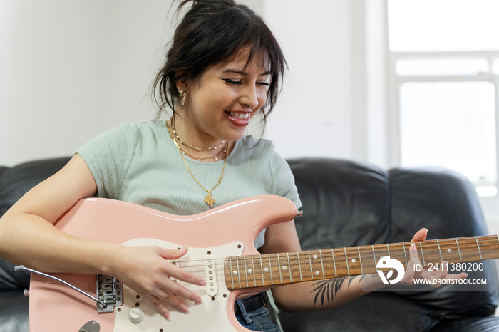 Young woman sitting on sofa and playing guitar