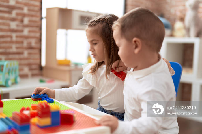 Adorable girl and boy playing with construction block pieces sitting on table at kindergarten