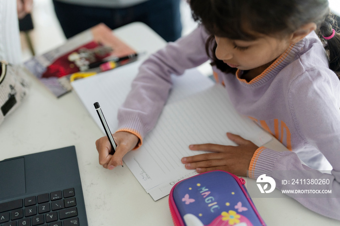 Little girl writing in notebook while doing homework