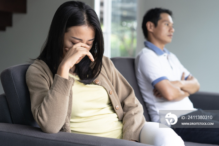 Asian couple having relation problem. Wife crying and sitting separate with her husband at home after quarrel.