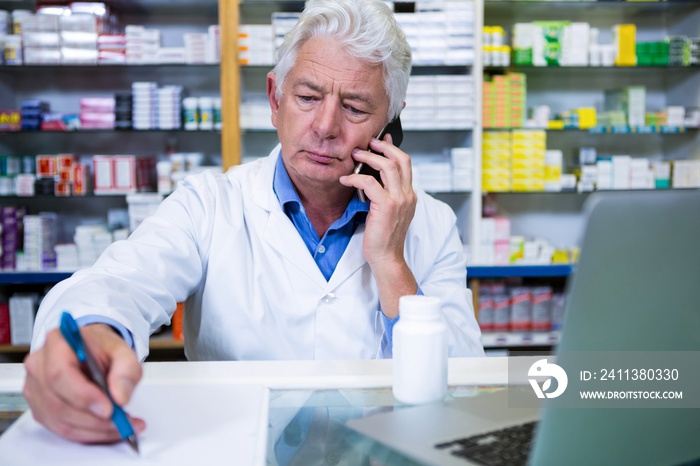 Pharmacist talking on mobile phone while writing prescriptions