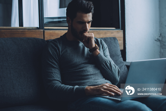 Handsome man with hand near mouth watching pornography on laptop in living room