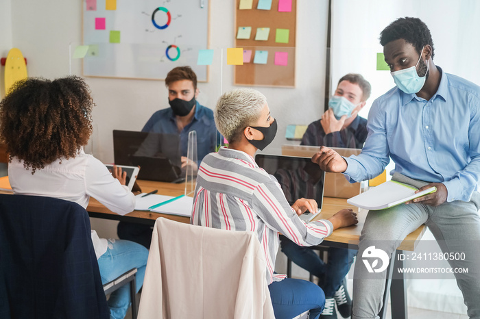 Young people working inside coworking office while wearing protective masks - Business and coworkers during coronavirus outbreak - Focus on african man face