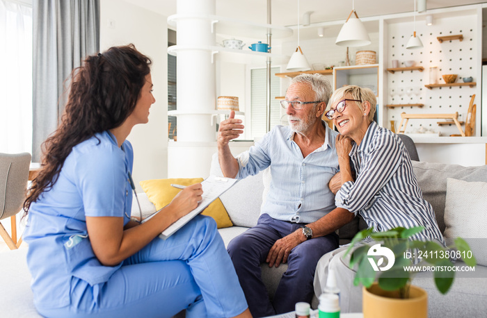 Female nurse talking to seniors patients while being in a home visit, senior couple signs an insurance policy.