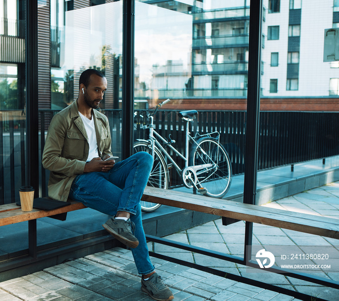 A young man sits at a bus stop and listens to music