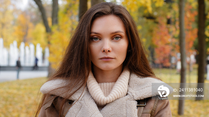 Close up female headshot portrait beautiful serious caucasian european appearance with flawless clean skin woman brunette millennial 20s girl upset offended lady stand in autumn park outdoors posing