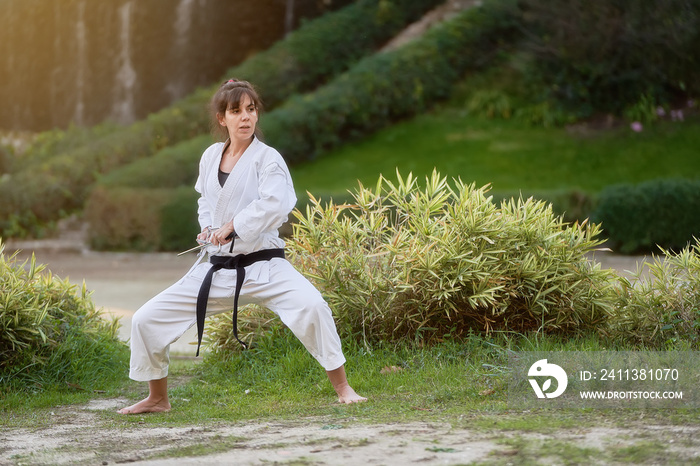 Young karate woman in fighting stance holding a pair of sai outdoors. High quality photo