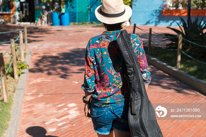 Rear view of young woman with guitar case walking on park