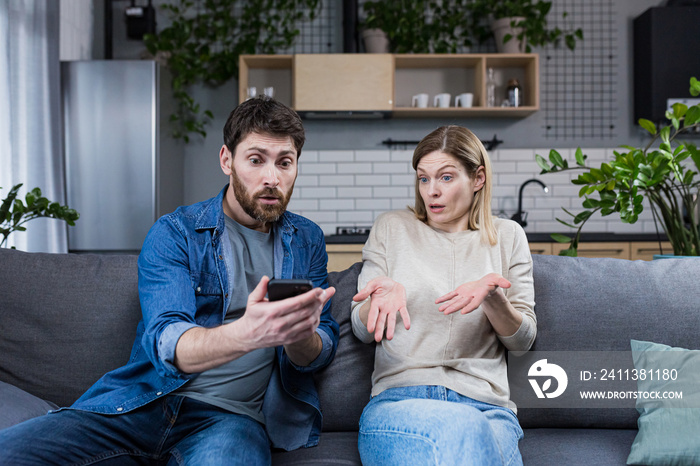 Family conflict at home. An angry man suspects a woman of treason, shouts at her, demands explanations, shows the phone, messages.