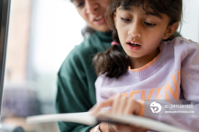 Mother and daughter reading book near window