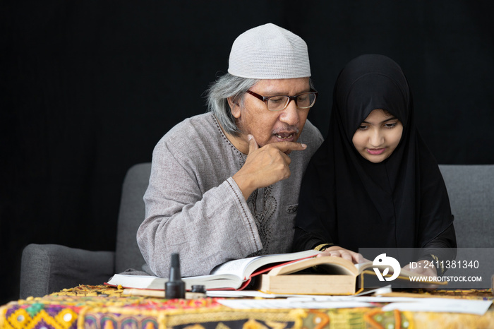 muslim father teaching his daughter about practicing reading textbook on black background