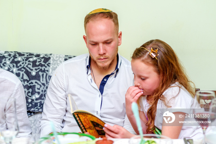 Family around the table for the traditional Passover dinner reading the Haggadah. Jewish family at the feast of Passover. Selective focus on man.