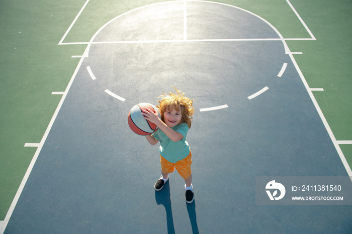 Cute smiling boy plays basketball. Kid shooting basketball ball and playing basketball. Healthy children lifestyle, outdoor on playground.