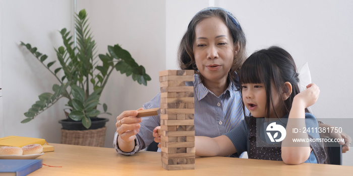 Happy moments of Asian grandmother with her granddaughter playing jenga constructor. Leisure activities for children at home.