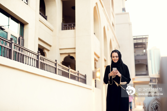 Muslim woman walking and typing message.