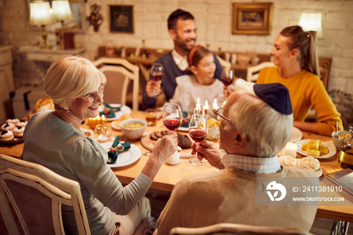 Happy senior couple toasts while celebrating Hanukkah and having family meal at dining table.