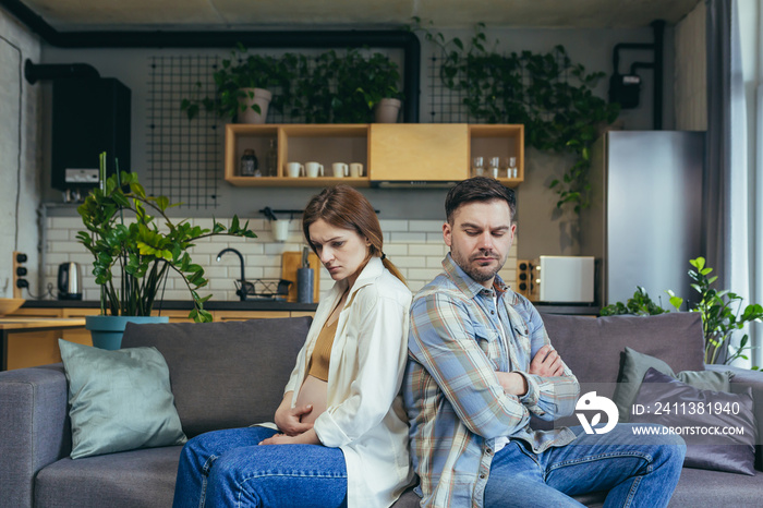 Family conflict. Young couple, pregnant woman and man sitting on sofa at home with their backs to each other. Do not talk, offended.