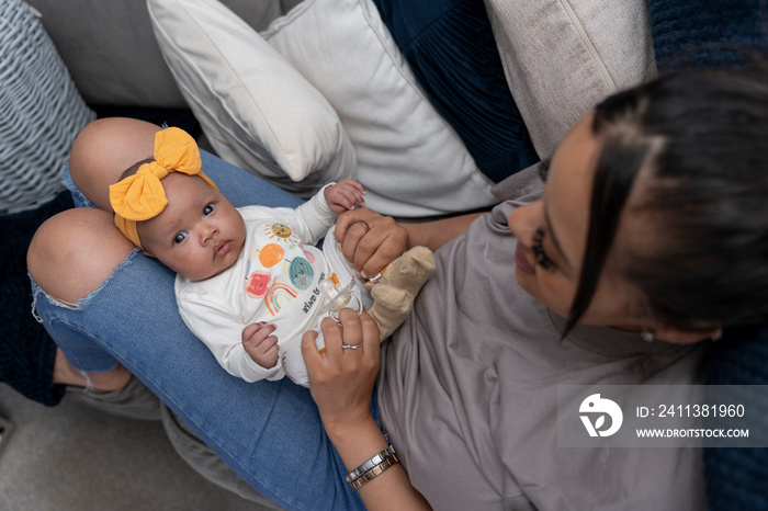 Mother relaxing with baby girl on sofa at home